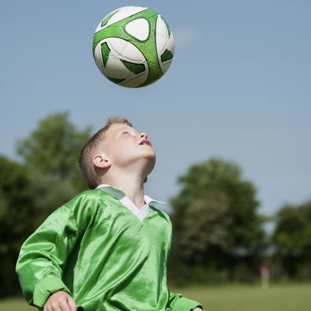 Ein Junge spielt alleine Fußball und trainiert Kopfbälle