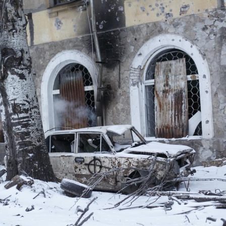 Ein zerstörtes Fahrzeug steht vor einem zerstörten Gebäude in der Ukraine, es liegt Schnee.