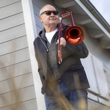 Nils Landgren mit roter Posaune sitzt im Sessel, um ihn herum die Funk Unit