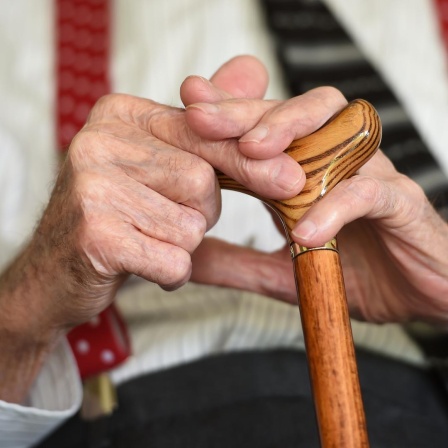 Ein älterer Parkinson-Patient, der einen Gehstock hält.