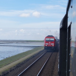 Blick aus dem Zugfenster einer Dampflok: Auf dem benachbarten Gleis ist eine rote Diesellok zu sehen.