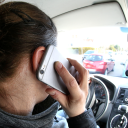 Eine Frau hält ein Mobiltelefon an ihr Ohr, während sie Auto fährt.