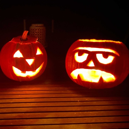 Drei geschnitzte Kürbisse leuchten zu Halloween im Garten.