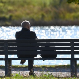 Mann sitzt auf einer Bank im Freien