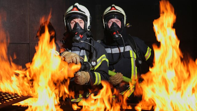 Zwei Feuerwehrmänner mit Atemschutzmaske umgeben von Flammen