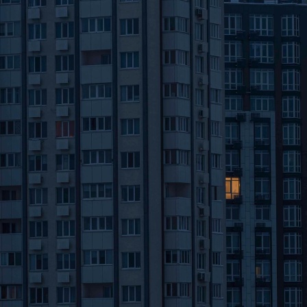 Ein Hochhaus in der Dunkelheit, nur aus wenigen Fenstern kommt Licht.