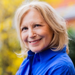 Porträtbild von Maren Kroymann, trägt eine blaue Bluse, lächelt in die Kamera