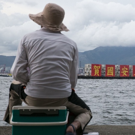 Angler in Hongkong betrachten ein vorüber fahrendes Schiff, welches auf roten Transparenten das von China erlassene neue Sicherheitsgesetz als nationalen Erfolg feiert.