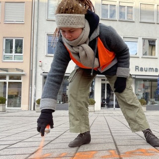 Eine Klimaaktivistin besprüht den Gehweg mit orangener Farbe.