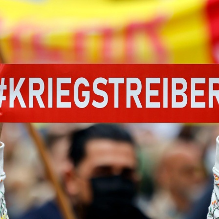 Ein Demonstrant gegen Kanzler Olaf Scholz hält ein Plakat mit dem Wort "Kriegstreiber!" in die Höhe auf der DGB-Veranstaltung am Tag der Arbeit auf dem Johannes Rau Platz. Düsseldorf, 01.05.2022