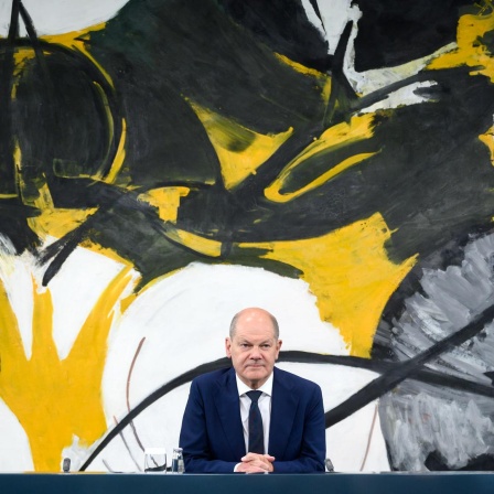 Stephan Weil, Olaf Scholz und Hendrik Wüst sitzen nebeneinander an einem Tisch. An der Wand hinter ihnen hängt ein großes modernes Gemälde.