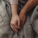 Zwei Hände ineinander verschränkt auf einer Decke