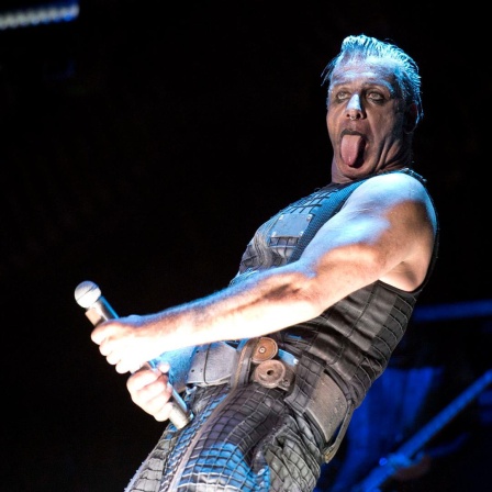 Der umstrittene Rammstein-Frontmann Till Lindemann steht geschminkt auf einer Bühne und macht mit dem Mikrofon eine Geste, die an einen Phallus erinnert. 