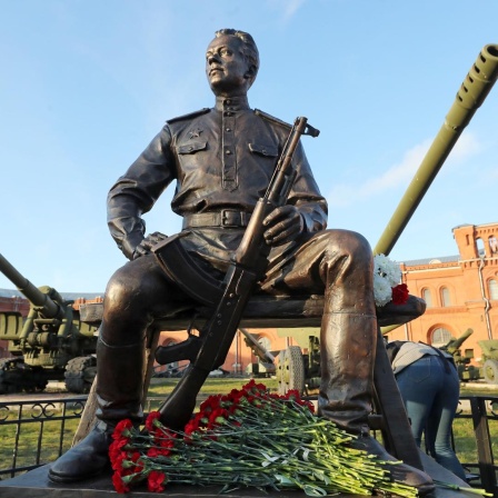 Eine Statue von Michail Kalaschnikow in St. Petersburg, vor der Statue liegen rote Rosen.