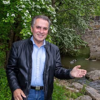 Naturschützer Claus-Peter Hutter zeigt mit der Hand auf einem Bach mit einer Steinbrücke.