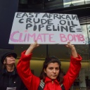 Eine junge Frau hält ein Schild in der Hand auf dem steht: "East African Crude Oil Pipeline = Climate Bomb". 