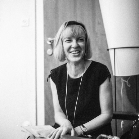 Schwarzweißaufnahme von Ingeborg Bachmann, die lachend in einem Salon sitzt