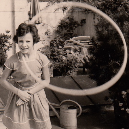 Ein Mädchen spielt mit einem Hula-Hoop-Reifen im Garten. 