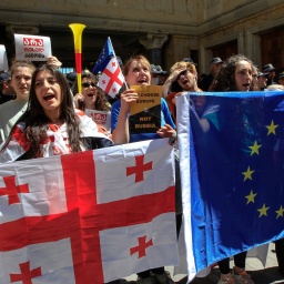 Demonstrantinnen zeigen Flaggen von Georgien und Europa bei einer Demonstration