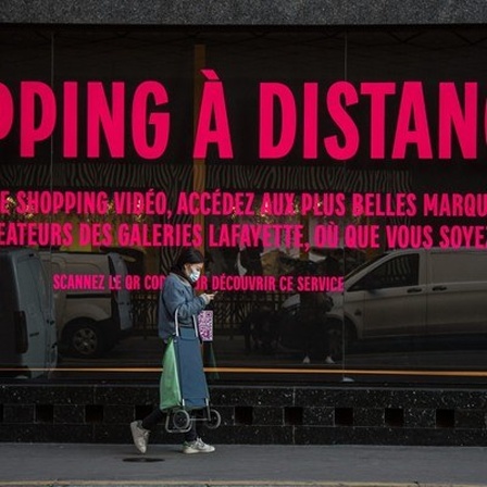 Frau läuft in Paris an einem Schaufenster vorbei, auf dem steht "Shopping à distance"