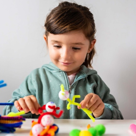 Lächelndes Mädchen spielt mit Pfeifenreinigern und Pompon-Spielzeug. 