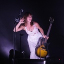 Die Feist steht mit ihrer Gitarre neben einem Mikrofon auf der Bühne.