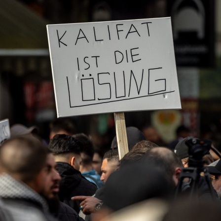 Teilnehmer einer Islamisten-Demo halten ein Plakat mit der Aufschrift "Kalifat ist die Lösung" in die Höhe. Foto vom 27.04.2024