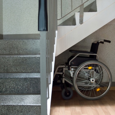 Ein Rollstuhl steht am unteren Treppenabsatz eines Treppenhauses.