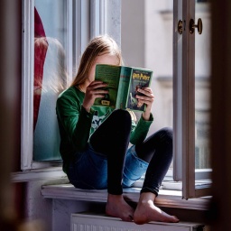 Ein Mädchen liest ein "Harry Potter" Buch, sie sitzt auf einer Fensterbank.