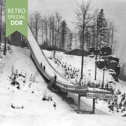 Sprungschanze Klingenthal, schneebedeckt, drei Menschen mit Skiern laufen die Schanze rauf