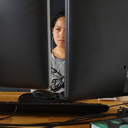 Eine Frau sitzt hinter zwei Computer-Bildschirmen.