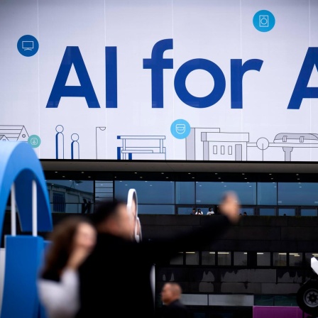 An einem Samsung Stand auf der IFA Berlin im Jahr 2024 steht in großen Buchstaben "KI for all" geschrieben. Davor sind in der Unschärfe einige Messebesucher zu sehen.