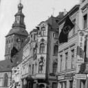 Historisches Bild mit Hakenkreuzfahnen in einer Straße mit Kirche im Hintergrund.