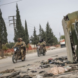 Syrische Oppositionskämpfer fahren südlich von Hama, Syrien, an einem beschädigten Regierungsfahrzeug vorbei.