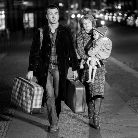 Filmszene aus &#034;Lieber Thomas&#034;: Thomas Brasch (Albrecht Schuch) geht mit seiner Frau (Jella Haase) die Straße entlang. Die Frau trägt das gemeinsame Kind (Olivia Mill), Brasch trägt zwei Koffer.