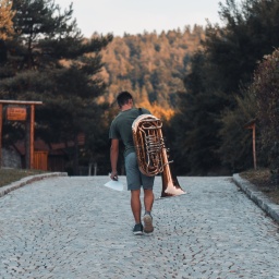 Mann läuft mit Tuba einen Weg entlang, Ansicht von hinten