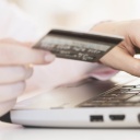 Eine Frau hält eine Kreditkarte in der Hand und tippt auf der Tastatur eines Laptops.