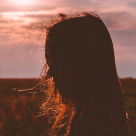 Eine junge Frau im Profil, Wiese und Sonnenuntergang im Hintergrund.