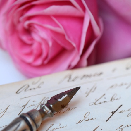 Federhalter mit Schreibfeder auf Buch mit alter Handschrift: Liebesbriefe sind Zeugnisse ihrer Zeit und Gesellschaft. Hieß es früher: "Ich liebe Dich", werden heute Emojis mit Herzchen und Küsschen gesendet.