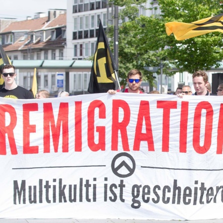Demonstranten der identitären Bewegung mit Bannern und Transparent auf dem steht "Remigration, Multikulti ist gescheitert" (Bild: IMAGO / Deutzmann)