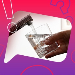Eine Hand hält ein Glas unter einen laufenden Wasserhahn.