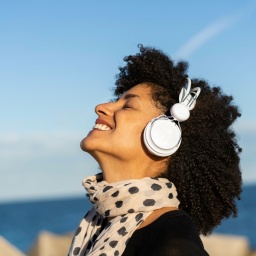Eine Frau hört sich fröhlich Musik über Kopfhörer am Meer an.