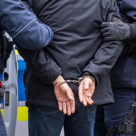 Polizisten führen einen Mann in Handschellen ab.