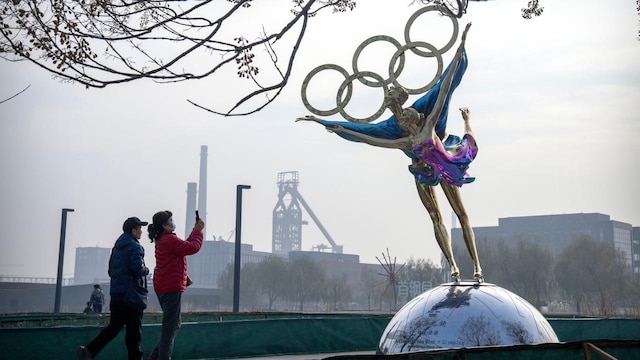 Besucher fotografieren eine Statue von Eiskunstläufern mit den olympischen Ringen in einem Park in der Nähe des Sitzes des Pekinger Organisationskomitees für die Olympischen Spiele (BOCOG).