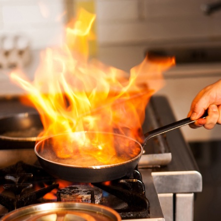 Ein Koch kocht mit Flamme in einer Bratpfanne auf einem Küchenherd.