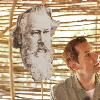 Malte Arkona betrachtet Fotografien von Brahms (links) und Dvořák (rechts)