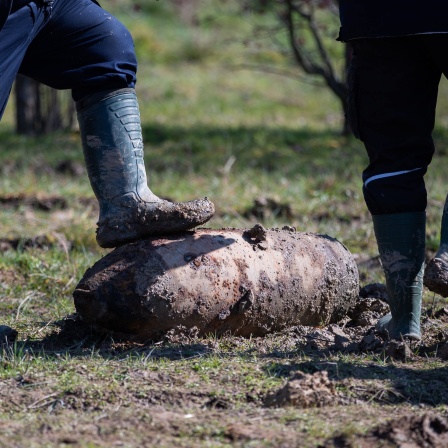 Zwei Mitarbeiter des Kampfmittelbeseitigungsdienstes stehen neben einer entschärften britischen Fliegerbombe auf einer Wiese.