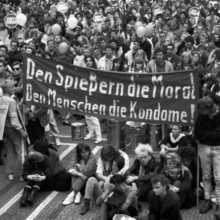 Eine Menschenmenge demonstriert unter em Motto  "Gegen Aids - für Vernunft" in München. In der Bildmitte ist ein Transparent mit der Aufschrift "Den Spießern die Moral, Den Menschen die Kondome!" zu sehen.