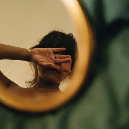 Spiegelbild einer jungen Frau, die ihr Gesicht mit der Hand bedeckt.
