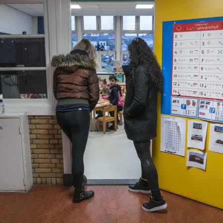 Zwei Frauen stehen in der offenen Eingangstür eines Klassenraums und schauen hinein zu den Grundschülern.